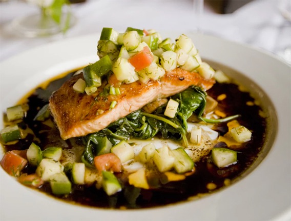 grilled salmon with chopped up pinnaples on top, sitting on top of spinnach and sesame glaze