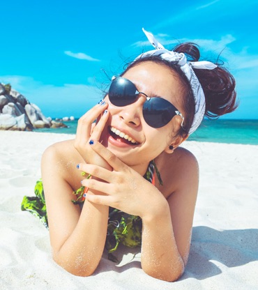 Similing girl with bandana and sunglasses laying on a beach.