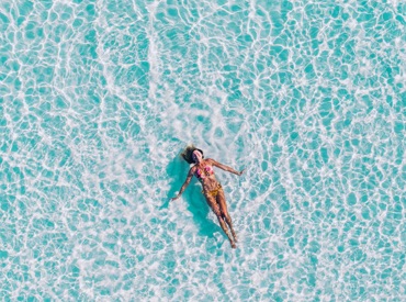 Woman floating across light blue ocean